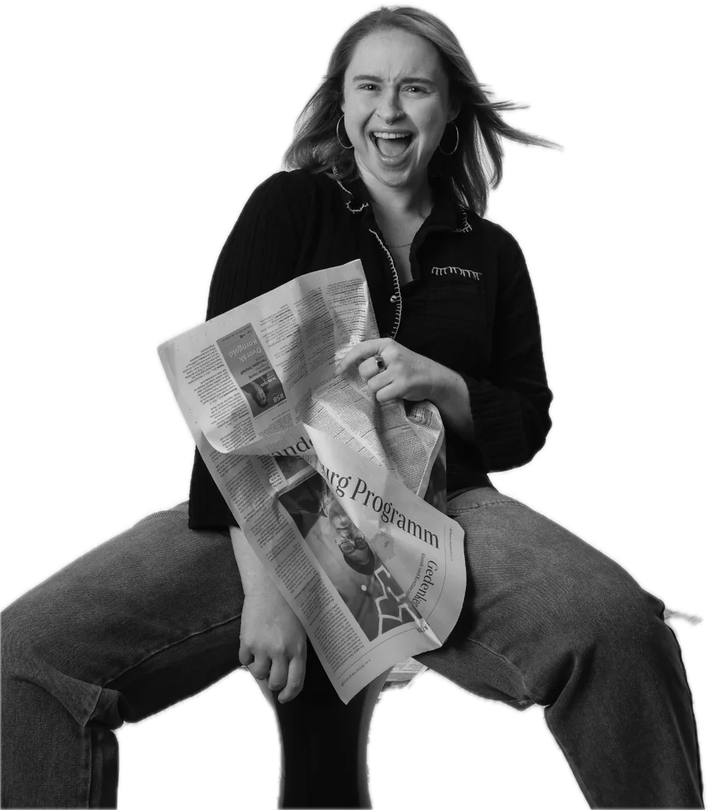 Emily perched on a stool, laughing open-mouthed and clutching a crumpled newspaper