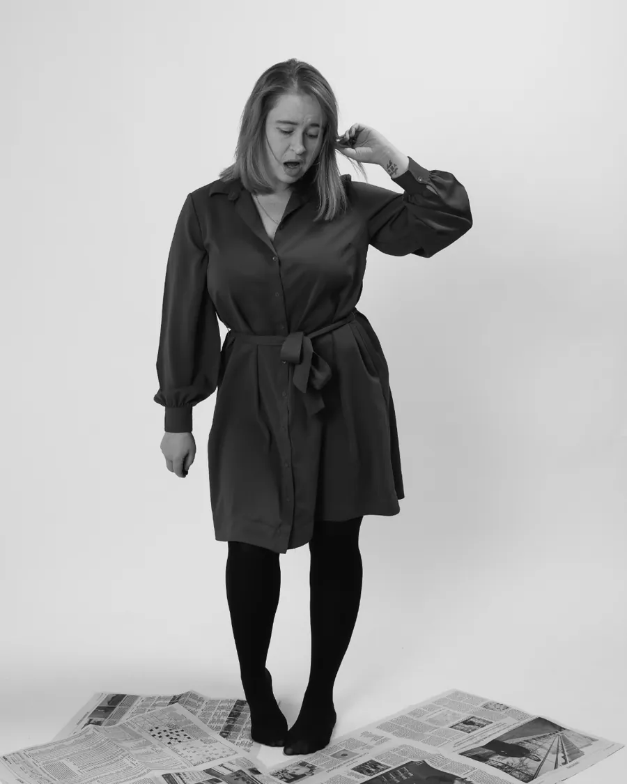 Emily standing on newspapers, tugging her hair and looking down, mid-sigh